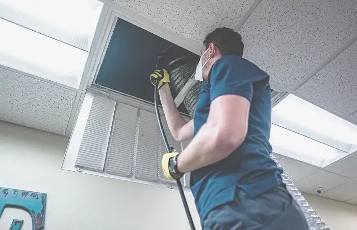 Technician cleaning a ceiling air duct vent